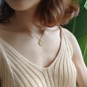 Golden coin pendant necklace for women on a model with beige knitwear and green plants