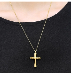 Nahaufnahme eines goldenen Kreuzanhängers mit Flügeldetails auf einem schwarzen Shirt
