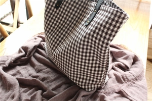Detail of checkered canvas tote bag with leather strap and metal rivet reinforcement