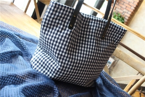 Detail of blue checkerboard canvas tote bag with brown leather handle and brass rivets