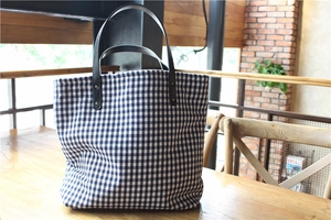 Detail of blue and white plaid tote bag with brown leather handles and metal rivets
