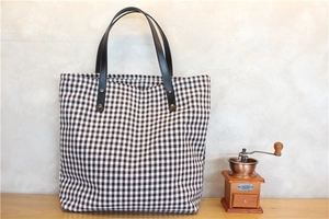 Close-up of small plaid tote bag with brown leather handles and metal rivets on wood
