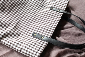Detail of gingham tote bag with brown checkered fabric and leather strap with gold rivets