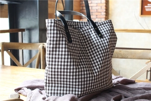 Detail of grid canvas tote bag with black leather straps and metal rivet reinforcement