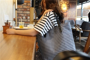 Blue and white gingham tote bag with black leather straps on a wooden table in a cafe