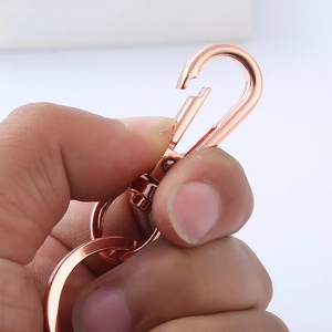 Close-up of a hand holding a rose gold metal spring clip for keychains and bags