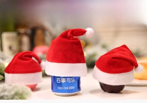 Mini red velvet Christmas hats decorating an apple and soda can in a cozy festive setting