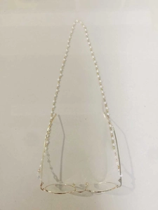 Detail view of white pearl eyewear chain and gold round frame glasses on a plain background