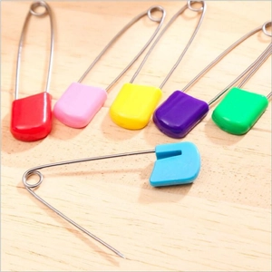 Macro detail of multi-colored plastic safety pins and knitting stitch markers on wood