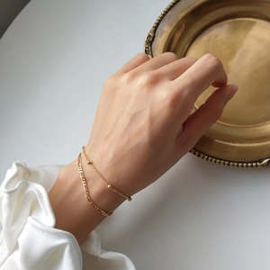 Detail of layered gold beaded and Figaro chain bracelet worn on a female wrist