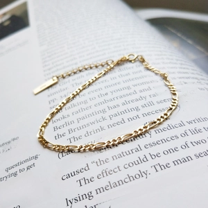 Detail of a gold Figaro chain bracelet with lobster clasp on a vintage book