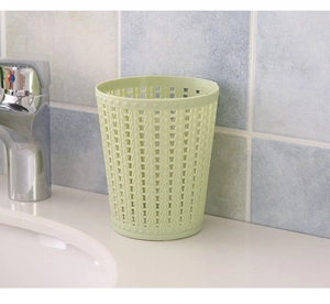 Detailed close-up of light green hollowed-out plastic waste bin on a white bathroom counter