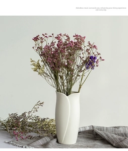 Detail of white ceramic vase with petal design and dry flowers on linen fabric
