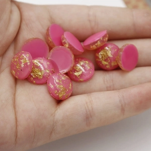 Macro detail of 12mm pink resin cabochons with gold foil flecks held in hand