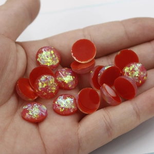Detail of 12mm oval red synthetic opal stones with glitter flakes held in hand