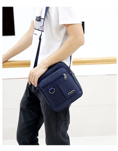 Close-up of navy blue oxford fabric crossbody bag with zip pocket and metal D-ring detail