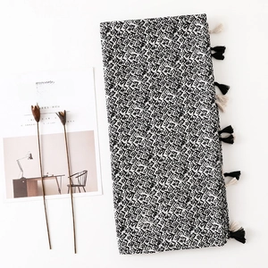 Détail d'un châle imprimé géométrique noir et blanc avec glands sur un décor minimaliste