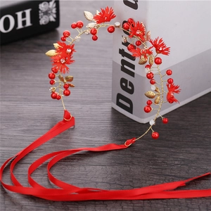 Close-up of bridal headband with red flowers, gold leaves, and crystals on a wood surface