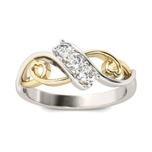 Macro detail of two-tone gold ring featuring three clear stones and hollow heart patterns