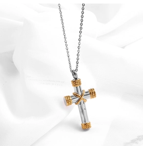 Close-up of silver cross perfume urn pendant with gold rope details on white fabric