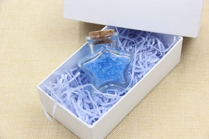 Star shaped glass bottle with cork stopper and blue crystals inside a gift box