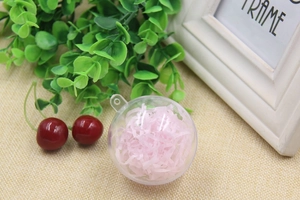 Close-up of a clear plastic ornament ball filled with pink shredded paper on a woven mat