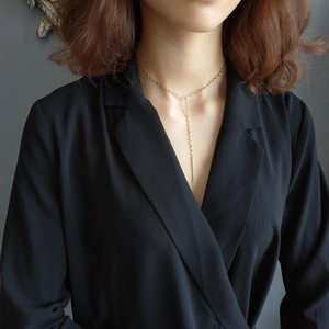 Detail of a minimalist gold Y-shaped long necklace with a sleek metal bar pendant on a model