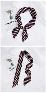 Detail of red and black striped narrow silk scarf tied in a bow on a white fabric