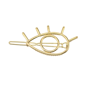 Macro shot of a golden metal eye-shaped hair clip featuring detailed eyelash accents