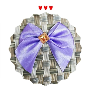 Detail of purple satin bow hair accessory with orange gemstone on a woven mat