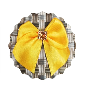 Detail of yellow satin bow hair accessory featuring a square amber rhinestone center