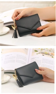Close-up of black leather wallet with metal heart charm and tassel held by a model