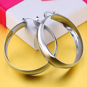Polished silver wide hoop earrings in stainless steel on a vibrant yellow background