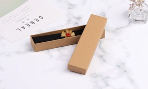 Brown kraft paper jewelry box with black velvet lining featuring a gold floral brooch