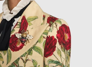 Close-up of vintage bee brooch with pearls and red-blue stripes on floral blazer