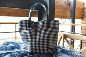 Detail of black and white gingham tote bag with leather straps and metal rivets