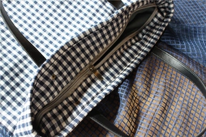 Close-up of blue gingham canvas tote bag featuring a metal zipper and black leather handles