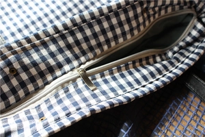 Detailed macro view of the zipper closure and blue-white plaid fabric texture of the bag