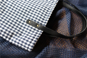Detail of blue plaid canvas tote with black leather handle and vintage metal rivets