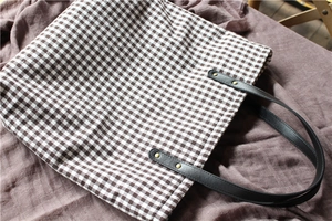Close-up of brown checkered canvas tote bag with black leather straps and gold rivets