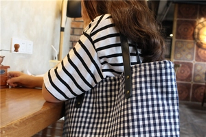 Detail of blue and white checkered canvas tote bag with black leather handle and brass rivets