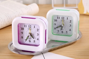Close-up of purple and green square plastic alarm clocks on a silver tray over a wood desk
