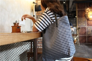 Blue plaid canvas tote bag with black leather straps shown in a cozy vintage cafe