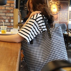 Blue and white checkered fabric tote bag with black leather straps in cafe setting