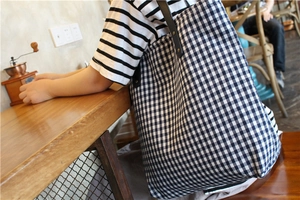 Detail of checkered canvas tote bag with black leather straps and gold rivets in a cafe