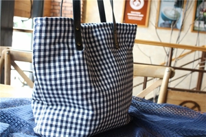 Detail of navy gingham canvas tote bag featuring leather handles and brass rivet accents