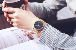 Close-up of a men's Milanese mesh strap watch worn while holding a coffee cup