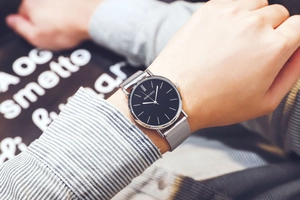 Detail of minimalist quartz watch with black dial and silver mesh band on wrist