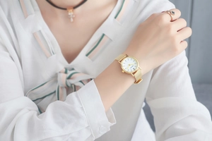 Lifestyle shot of a woman wearing a gold mesh strap watch with a minimalist white dial