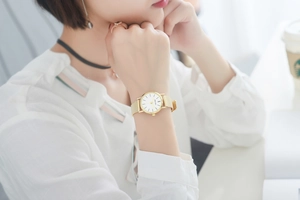 Elegant gold mesh strap watch with a white dial shown on a woman's wrist